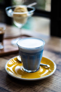 Hot milk with butterfly pea mixed and milk froth on the top of glass, decorate with yellow disk.