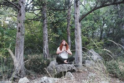 Young woman sitting on rock against tree trunk in forest