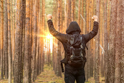 Man in hooded shirt clenching fists against trees