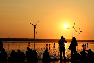 Silhouette people on shore against sky during sunset