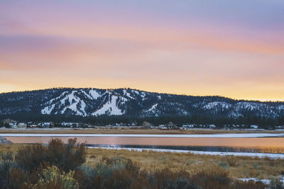 Scenic view of lake by snowcapped mountains against sky during sunset