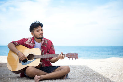 Young man playing guitar on beach