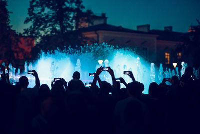 Rear view of crowd photographing illuminated fountain at night