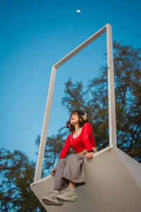 Low angle view of woman listening music against blue sky