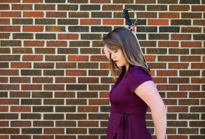 Side view of young woman holding sword while standing by brick wall