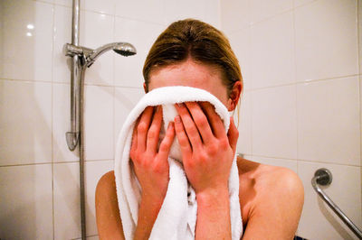 Close-up of woman rubbing towel on face while standing in bathroom