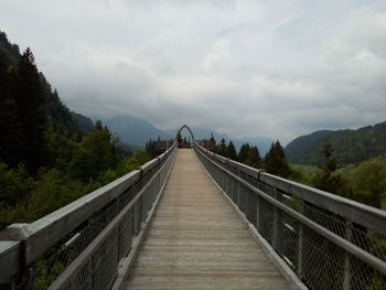 Footbridge leading towards mountains against sky
