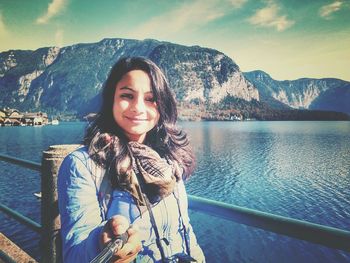 Portrait of smiling young woman standing by lake against mountains