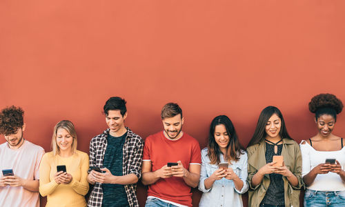 Full length of young woman using mobile phone against orange wall