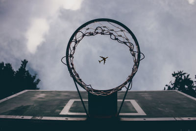 Directly below shot of airplane flying seen through basketball hoop against sky