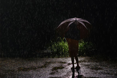 Rear view of person standing on wet road during rainy season