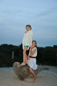 Portrait of happy siblings on wooden sculpture against sky at dusk
