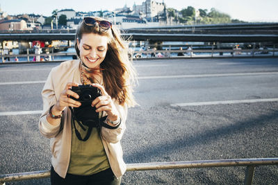 Portrait of smiling young woman using mobile phone in city