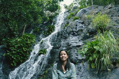 Portrait of smiling woman against waterfall in forest