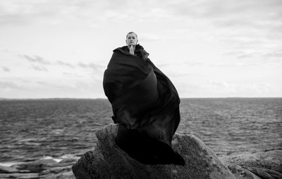 Portrait of woman standing on rock at beach against sky