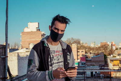 Portrait of young man with face mask in city against clear sky