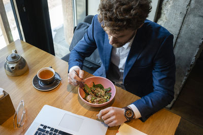 Businessman having salad while sitting with laptop at cafe