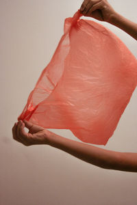 Cropped hand of person holding plastic bag over white background