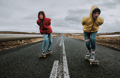 Full length of couple skateboarding on road against sky