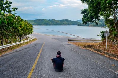 Rear view of man sitting on road against sky