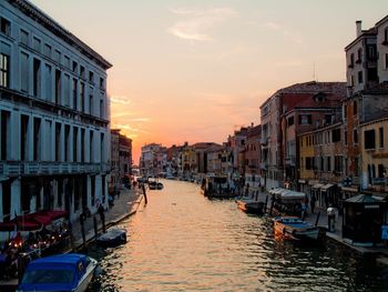 Boats in canal amidst buildings in city during sunset