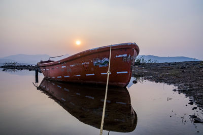 Abandoned boat moored on lake against sky during sunset