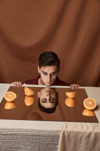 Man looking away with oranges on mirror against brown background