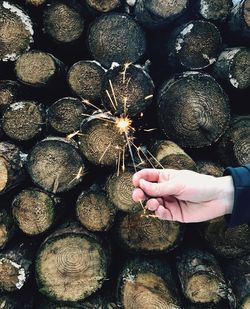 Cropped hand of woman holding sparkler by firewood