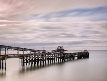 Pier in sea against cloudy sky