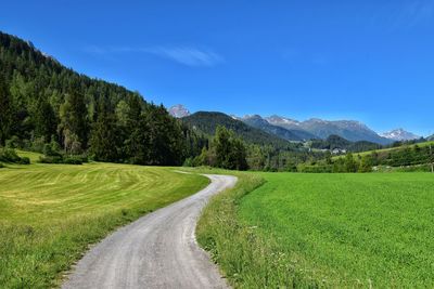 Road amidst field against clear blue sky