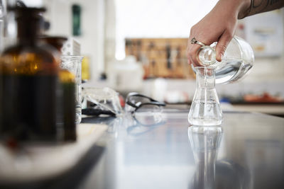 Cropped hand of female student pouring liquid solution in flask from bottle at laboratory