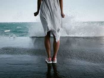 Low section of woman standing on wet beach