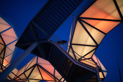 Low angle view of woman standing on footbridge against illuminated structure at dusk