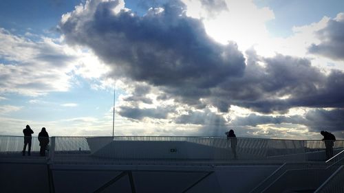 Silhouette people standing by railing in city against sky