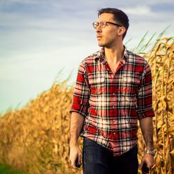 Young man looking away while standing on field against sky