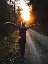 Rear view of woman with arms outstretched standing on dirt road in forest