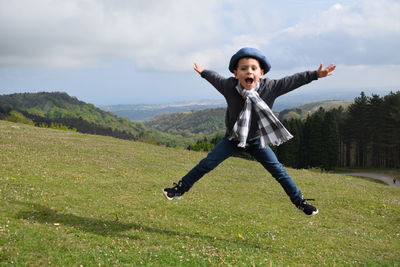 Full length portrait of boy jumping over grassy field against sky