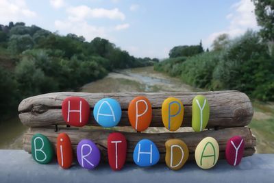 Happy birthday text with colored stones over two wooden pieces and natural background