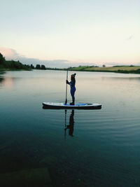 Man on boat in lake against sky during sunset