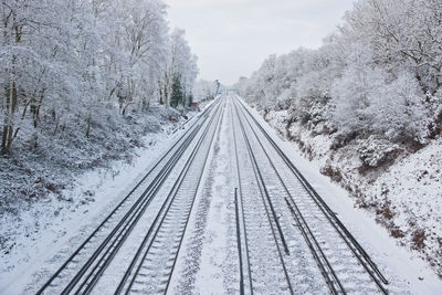 Railroad tracks by snow covered trees against sky