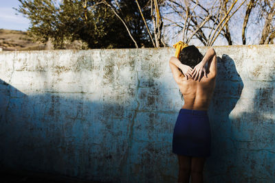 Rear view of shirtless woman standing against wall