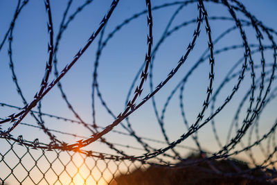 Close-up of barbed wire against sky during sunset
