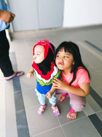 High angle view of cute sisters pouting on tiled floor