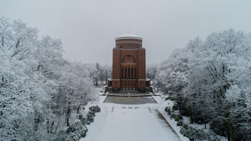 Snow covered field by building against sky