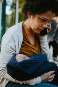 Woman listening over phone while holding baby boy standing by fence