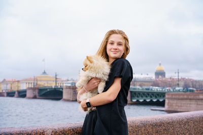 Young woman hugs spitz dog outdoors on embankment of city river in black