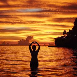 Silhouette woman standing by sea against sky during sunset