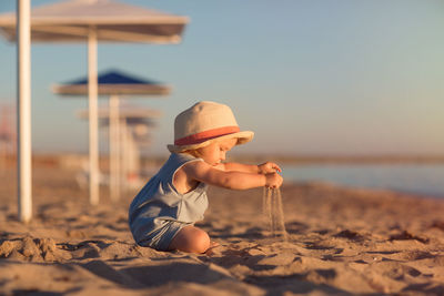 Boy wearing hat on sand at beach against sky