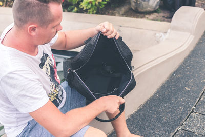 High angle view of man holding camera while sitting outdoors