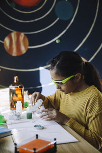 Motivated girl pouring chemical while doing scientific experiment at table